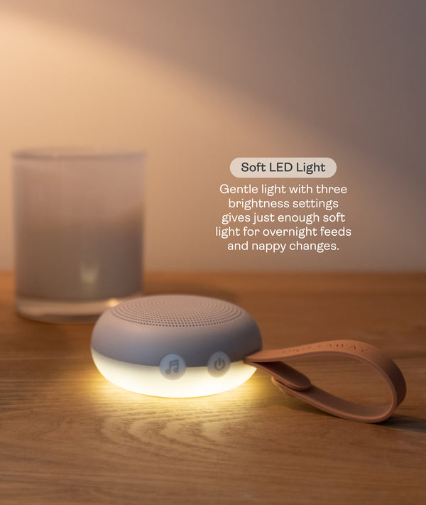 A portable White Noise Machine with a strap sitting on a wooden surface, casting a soft, warm LED light. Text overlay reads 