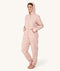 Barefoot woman standing against a white background wearing a hooded light pink floral Adult Sleep Onesie with her hands in the pockets.