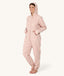 Barefoot woman standing against a white background wearing a hooded light pink floral Adult Sleep Onesie with her hands in the pockets.