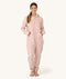 Woman standing barefoot facing forward in a light pink floral hooded Adult Sleep Onesie with hands in front pockets.