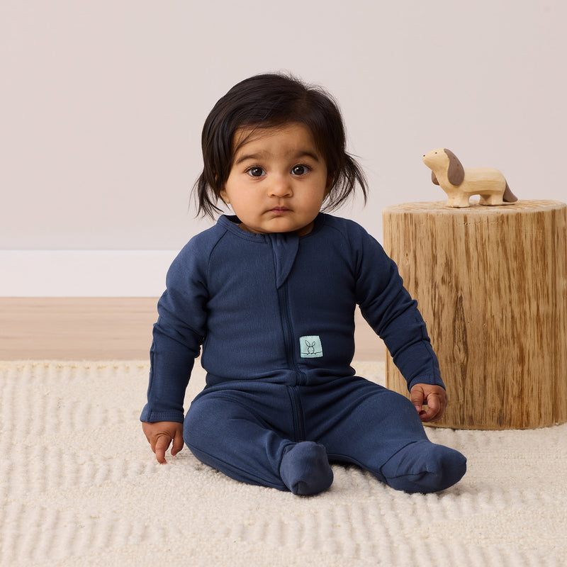 Infant wearing an ergoPouch long sleeve layer in navy blue, made from soft, natural fabric.