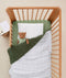 Shot of a cot complete with a ergoPouch Organic Toddler Pillow Case Midnight Stripe, a teddy bear wearing an doll sleep bag and a weighted blanket