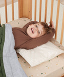 Toddler in bed lying on an ergoPouch Organic Toddler Pillow Case in Caramel Grid