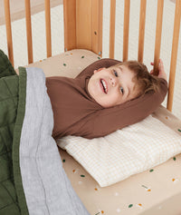 Preschool kid lying in a cot with an ergoPouch pillow, made from organic, non-toxic materials.