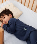 Toddler lying in a cot with an ergoPouch low-profile pillow, made from natural, non-toxic materials.