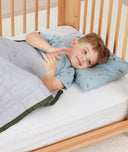 Little boy lying in bed on an ergoPouch low-profile pillow with protector, made from organic, non-irritating materials.