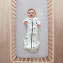 Baby lying in a cot wearing a Cocoon Swaddle Bag 2.5 TOG Clouds, with arms out