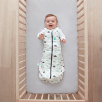 Baby lying in a cot wearing a Cocoon Swaddle Bag 2.5 TOG Clouds, with arms out