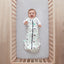 Baby lying in a cot wearing a Cocoon Swaddle Bag 2.5 TOG Clouds, with arms out