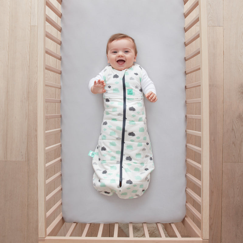 Baby lying in a cot wearing a Cocoon Swaddle Bag 2.5 TOG Clouds, with arms out