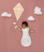 Newborn asleep in ergoPouch Cocoon Swaddle Bag 0.2 TOG Daydream, arms out sleeping, with a geometric kite and clouds