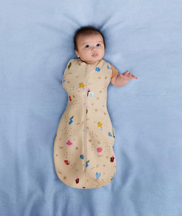 Newborn wearing an ergoPouch Cocoon Swaddle Bag 1.0 TOG Birthday Blobs with one arm out