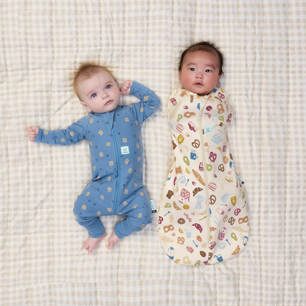 Baby swaddled in ergoPouch Cocoon Swaddle Bag 1.0 TOG in Bon Appetit with another baby lying beside in ergoPouch Long Sleeve Layer 1.0 TOG Petit Pretzel