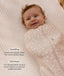 Smiling baby wrapped in a Cocoon Swaddle Bag lying on a grid-patterned sheet with text highlighting  swaddling benefit and TOG rating feature.