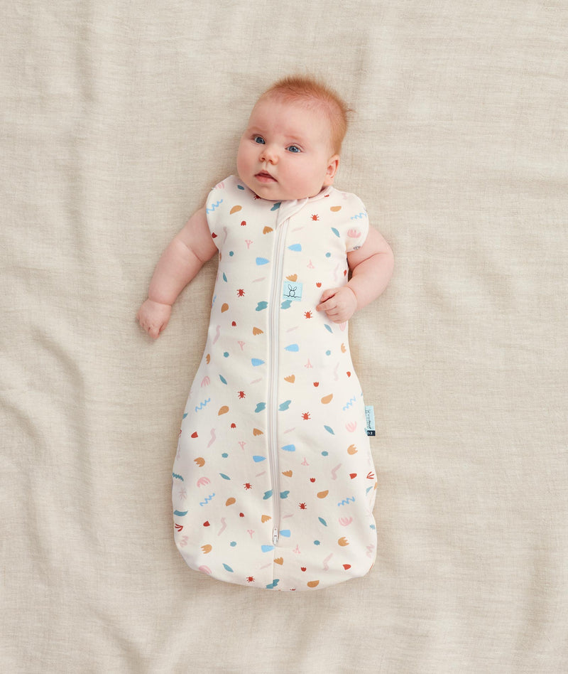 Baby wearing a Cocoon Swaddle Bag 1.0 TOG Desert Bloom,  transitioning into arms out sleeping