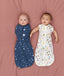 Two babies lying down, one being swaddled in an ergoPouch Cocoon Swaddle Bag 1.0 TOG Starbeam, the other, trainsitioned to arms out sleeping in ergoPouch Cocoon Swaddle Bag 1.0 TOG Daydream 