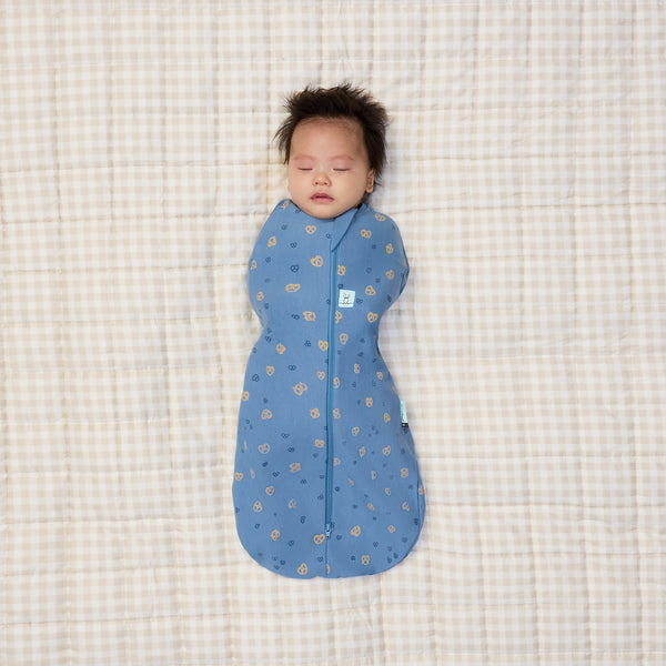 Newborn being swaddled in ergoPouch Cocoon Swaddle Bag 0.2 TOG in Petit Pretzel