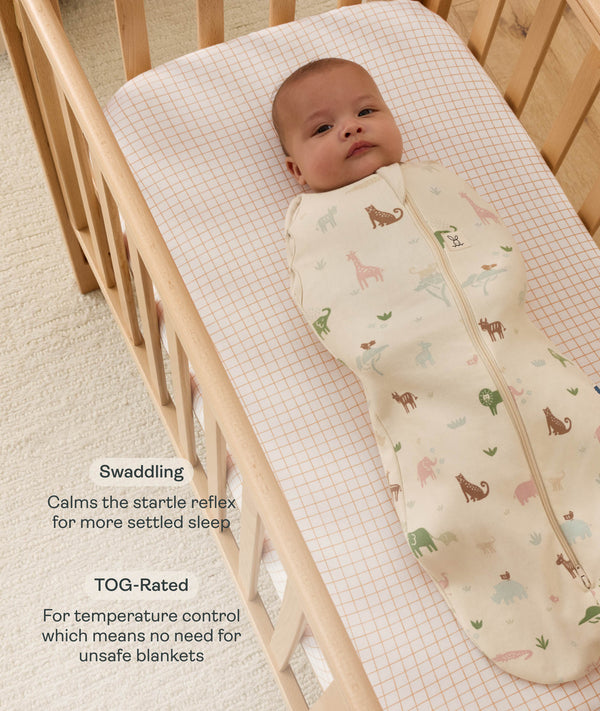 Baby lying in a wooden bassinet wearing a safari-themed Cocoon Swaddle Bag with text highlighting swaddling benefit and TOG rating feature.