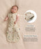 Baby lying on a cream-coloured blanket wearing a Cocoon Swaddle Bag with both arms out. On the right is a close-up inset and text highlighting press studs and a bell-shaped design.
