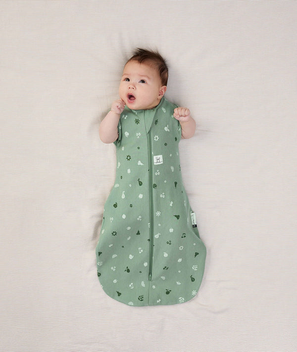 Newborn wearing an ergoPouch Cocoon Swaddle Bag 1.0 TOG Sweet Orchard with arms out