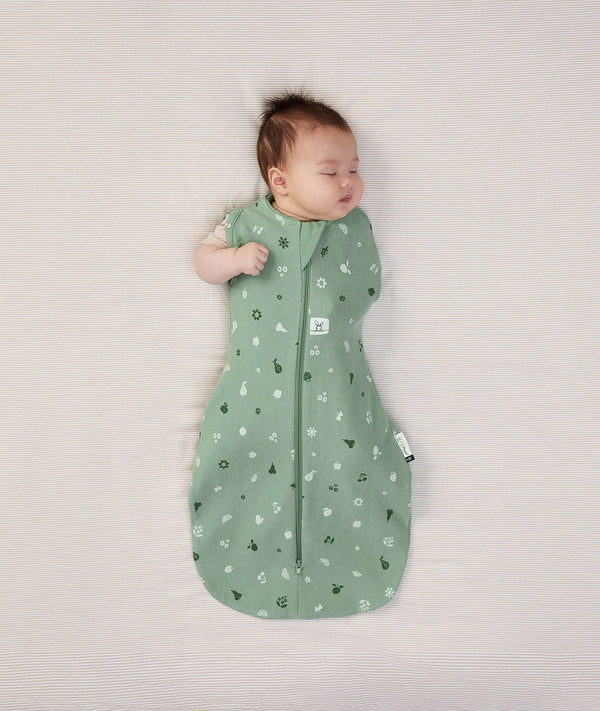 Newborn wearing an ergoPouch Cocoon Swaddle Bag 1.0 TOG Sweet Orchard with one arm out