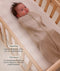 Baby lying in a wooden cot wearing a Cocoon Swaddle Bag with callouts on the left highlighting swaddling benefit and TOG rating feature.