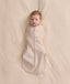 An overhead view of a baby swaddled in a patterned beige Cocoon Swaddle Bag, lying flat on a cream-colored blanket.