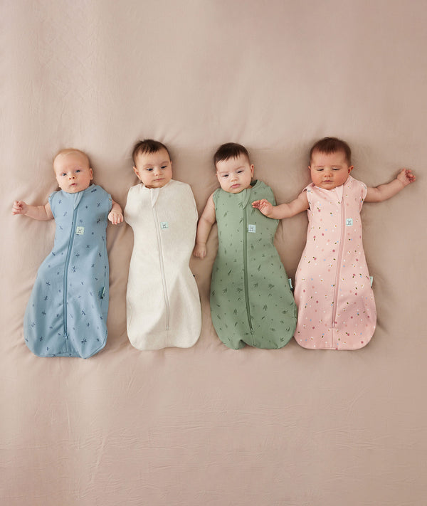 Four babies wearing an ergoPouch organic swaddle, featuring colourful, seasonal prints.