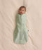Baby swaddled in a green floral Cocoon Swaddle Bag 1.0 TOG, lying on a cream-coloured blanket.