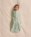 Baby swaddled in a green floral Cocoon Swaddle Bag 1.0 TOG, lying on a cream-coloured blanket.