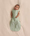 Baby lying on a cream blanket, wearing an ergoPouch Cocoon Swaddle Bag 1.0 TOG with both arms out.