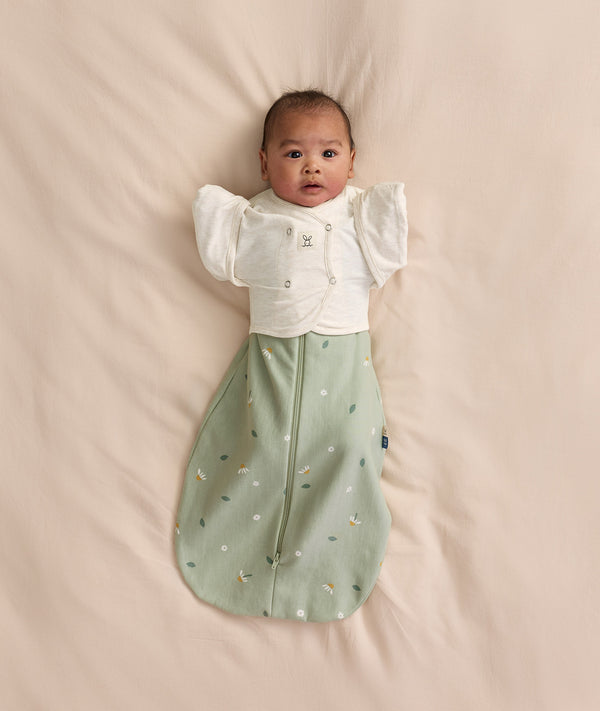 Baby wearing a sage green floral Cocoon Swaddle Bag layered with a white 