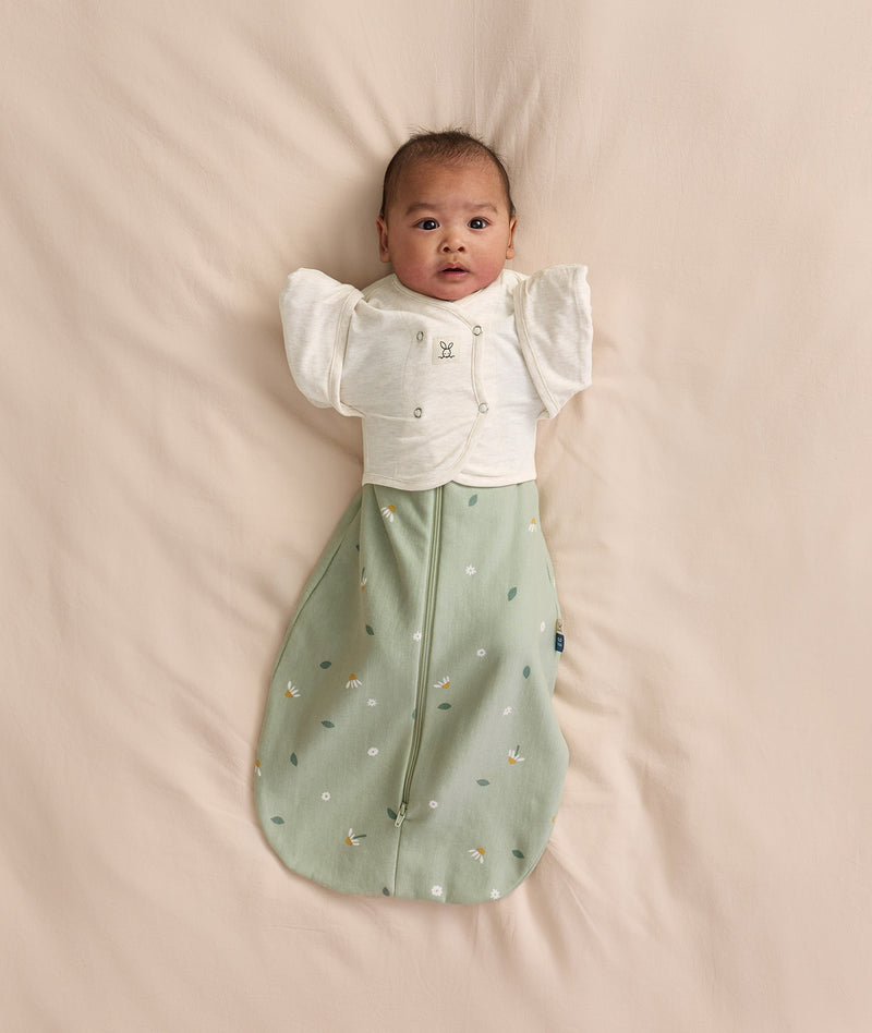 Baby wearing a sage green floral Cocoon Swaddle Bag layered with a white 