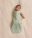 Baby wearing a sage green floral-patterned Cocoon Swaddle Bag with one arm extended out