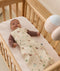 A baby wearing a brown long-sleeve romper and a safari-print Cocoon Swaddle Bag lying in a wooden crib.
