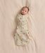 Baby lying on a cream blanket swaddled in a safari-patterned Cocoon Swaddle Bag 1.0 TOG.