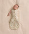A baby lying on a soft cream blanket in a safari-print Cocoon Swaddle Bag with one arm released.