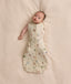 A baby lying on a soft cream blanket in a safari-print Cocoon Swaddle Bag with one arm released.