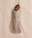 Baby lying on a cream blanket, swaddled in an ergoPouch Cocoon Swaddle Bag 1.0 TOG Taupe Marle