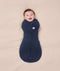 A smiling baby wrapped  in a dark blue Cocoon Swaddle Bag 2.5 TOG on a cream-coloured blanket