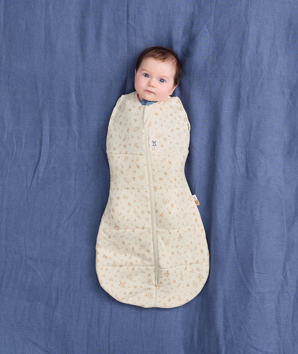 Baby lying on a blue fabric background, wrapped in a cream patterned Cocoon Swaddle Bag 2.5 TOG