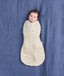 Baby lying on a blue fabric background, wrapped in a cream patterned Cocoon Swaddle Bag 2.5 TOG