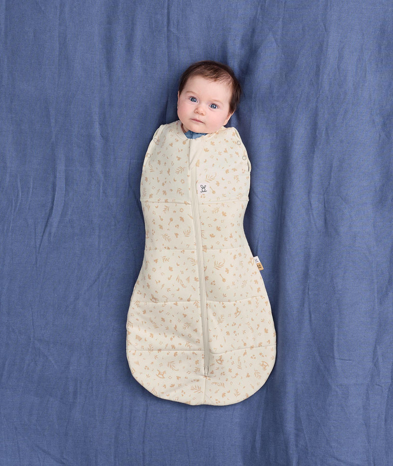 Baby lying on a blue fabric background, wrapped in a cream patterned Cocoon Swaddle Bag 2.5 TOG