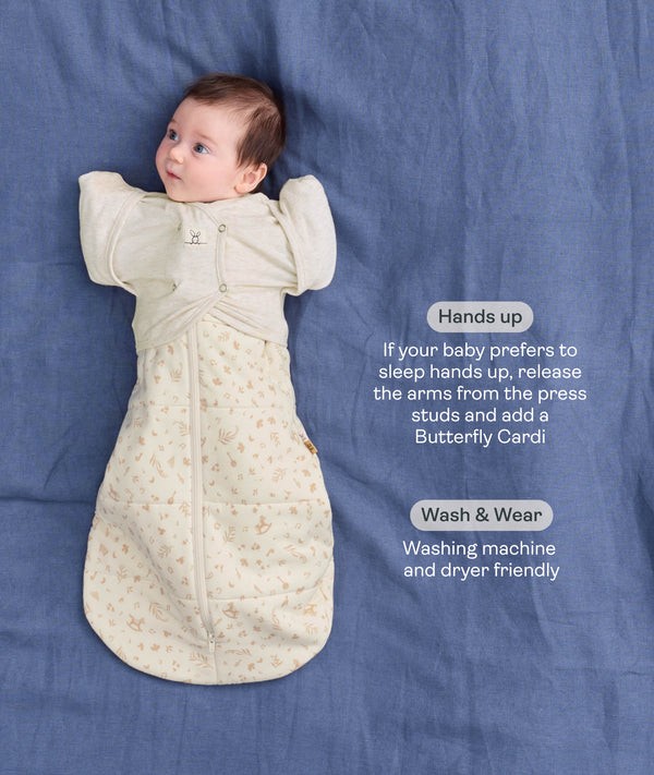 Product infographic showing a baby wearing a Cocoon Swaddle Bag paired with a Butterfly Cardi layer on a blue fabric background with text highlighting hands up sleeping and wash & wear friendly feature.