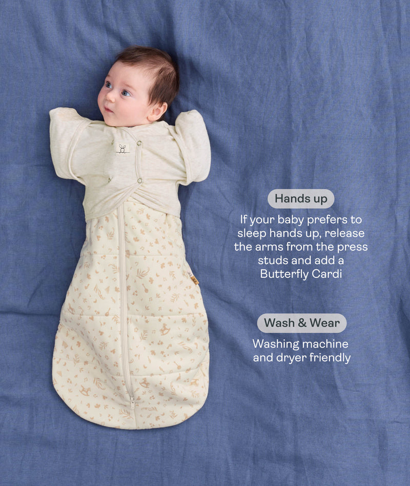 Product infographic showing a baby wearing a Cocoon Swaddle Bag paired with a Butterfly Cardi layer on a blue fabric background with text highlighting hands up sleeping and wash & wear friendly feature.