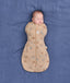A newborn sleeping peacefully while wrapped snugly in a tan, patterned Cocoon Swaddle Bag 2.5 TOG on a blue fabric background.