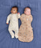 Two babies lying on a blue fabric background wearing ergoPouch sleepwear. One wearing a Long Sleeve Layer in Lullaby and the other one is wrapped in a 2.5 TOG Cocoon Swaddle Bag Melody.