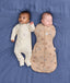 Two babies lying on a blue fabric background wearing ergoPouch sleepwear. One wearing a Long Sleeve Layer in Lullaby and the other one is wrapped in a 2.5 TOG Cocoon Swaddle Bag Melody.