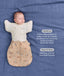 A baby sleeping peacefully on a blue fabric background, wearing a tan patterned Cocoon Swaddle Bag paired with a cream Butterfly Cardi. Text overlays highlight 