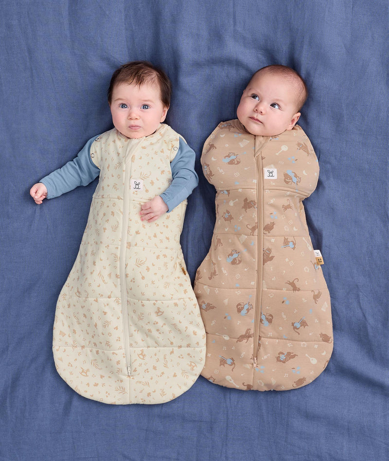 Two babies lying side by side wearing ergoPouch Cocoon Swaddle Bag in Lullaby and Melody.